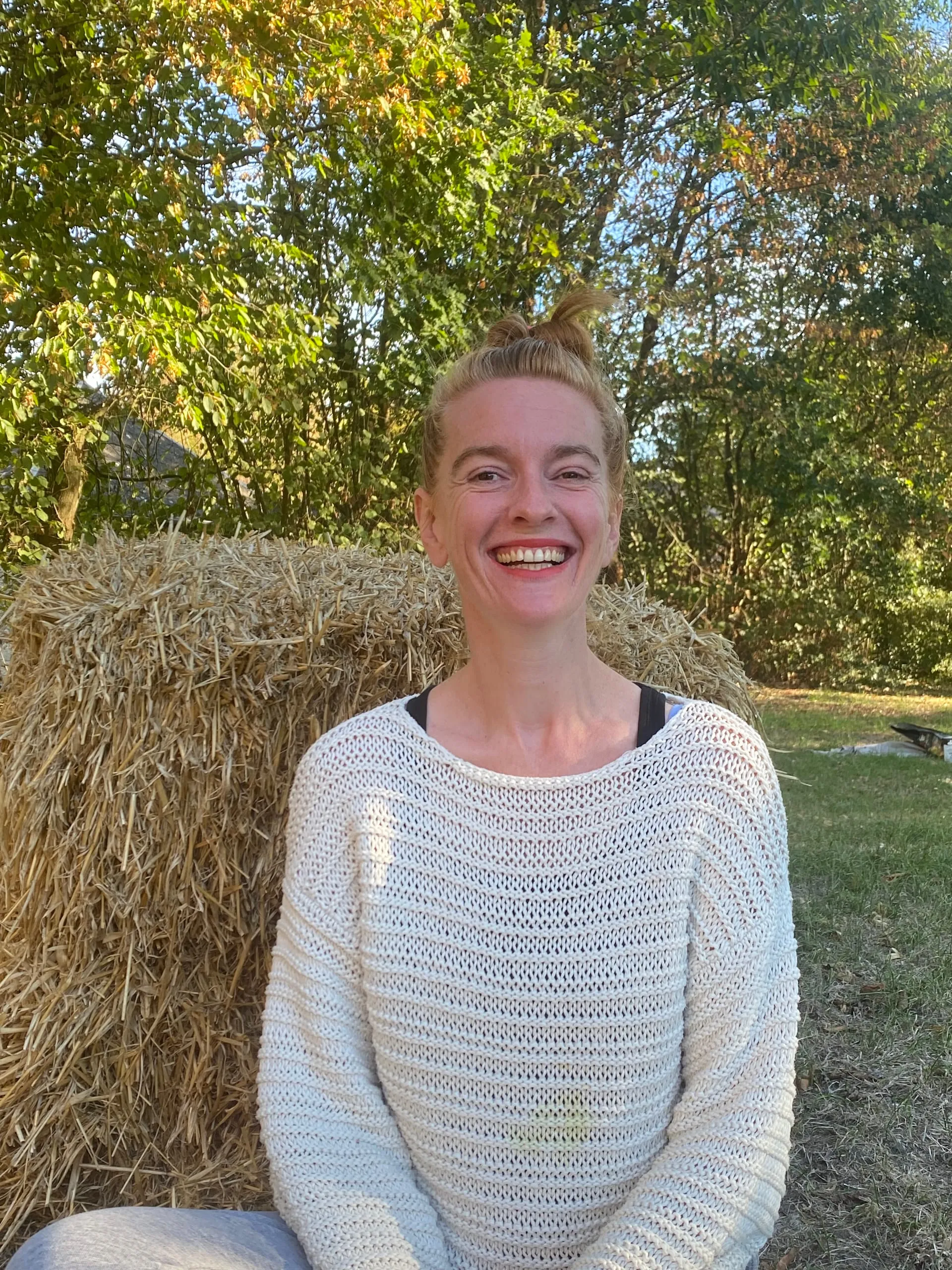 Diane de Sagazan souriante en pull blanc devant une botte de paille et des arbres